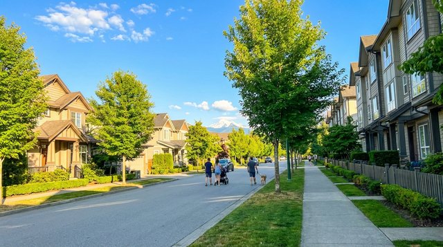 Candid summer streetscape in Newton, Surrey, BC — tree-lined residential street with pedestrians and cyclists, shot on Samsung S25 Ultra for AG. Song REALTOR®